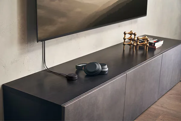 a headphone lying on a wooden table and a TV hanging on the wall